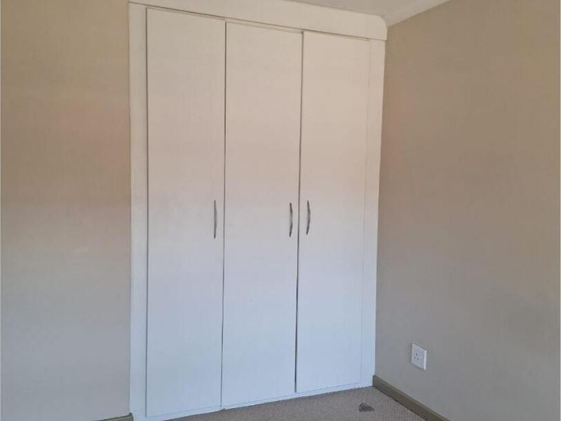 A clean, empty bedroom featuring neutral walls, carpeted flooring, and a functional white built-in wardrobe.