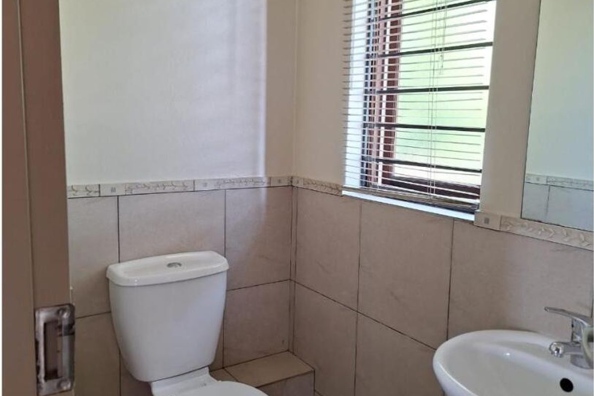 A functional guest bathroom featuring a pedestal basin, toilet, tiled finishes, and a window with venetian blinds.