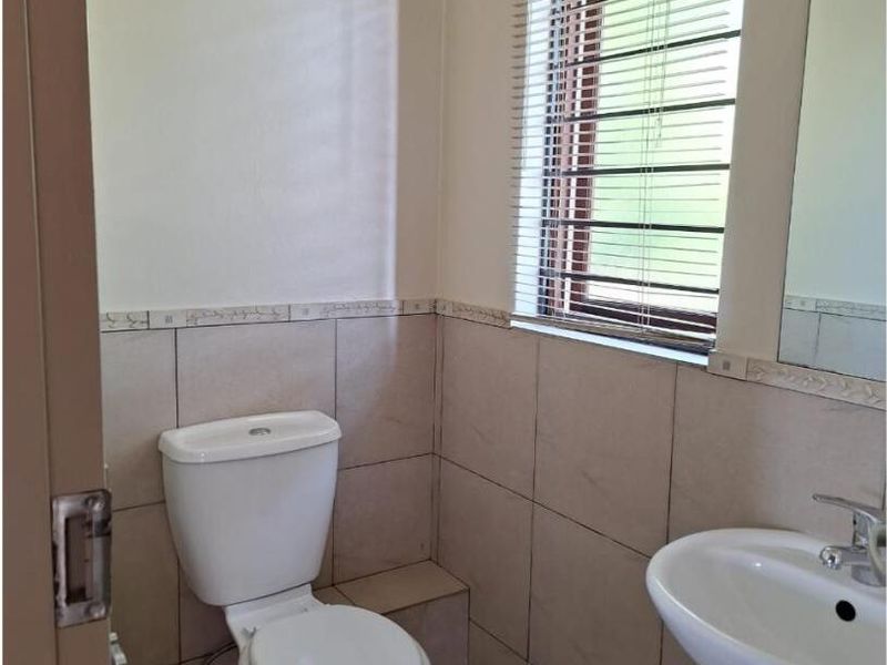 A functional guest bathroom featuring a pedestal basin, toilet, tiled finishes, and a window with venetian blinds.