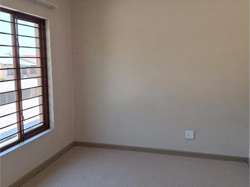A clean, empty bedroom featuring neutral walls, carpeted flooring, and a window fitted with security bars.