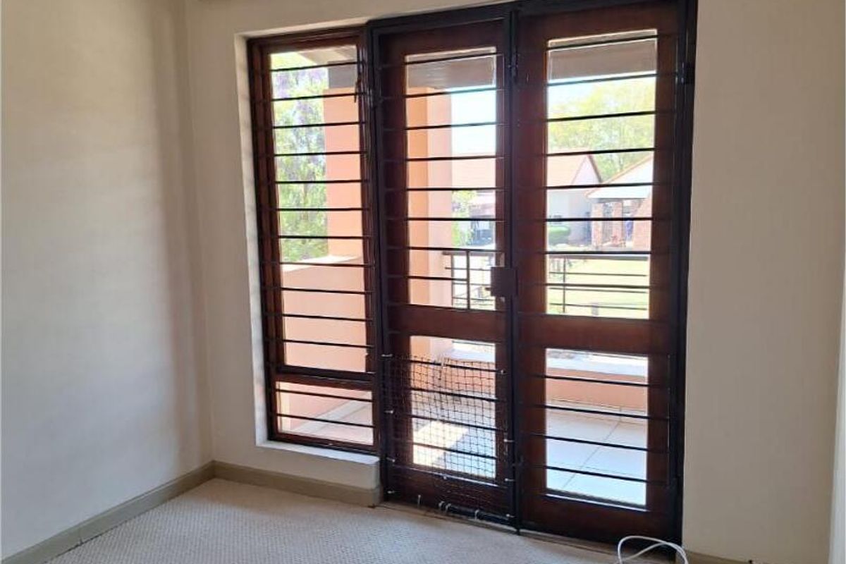 An empty bedroom featuring carpet flooring and a timber-framed glass door with an integrated security gate leading to the exterior.