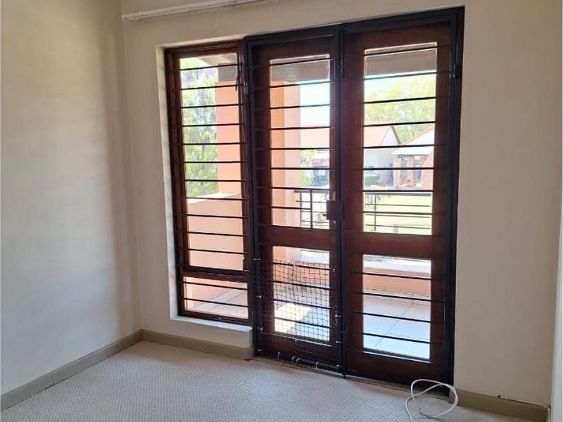 An empty bedroom featuring carpet flooring and a timber-framed glass door with an integrated security gate leading to the exterior.