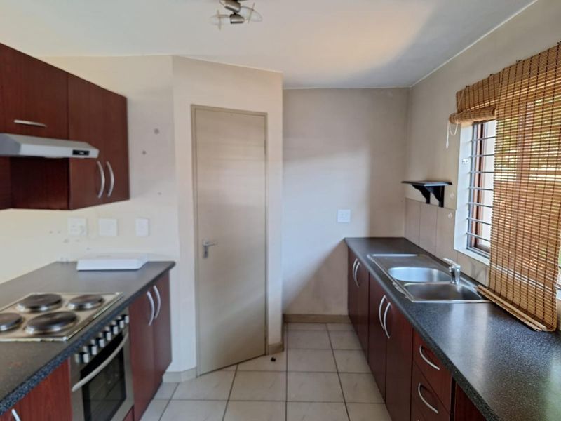 A functional kitchen featuring dark wood cabinetry, laminate countertops, a stainless steel sink, and a built-in electric stove with an extractor fan.