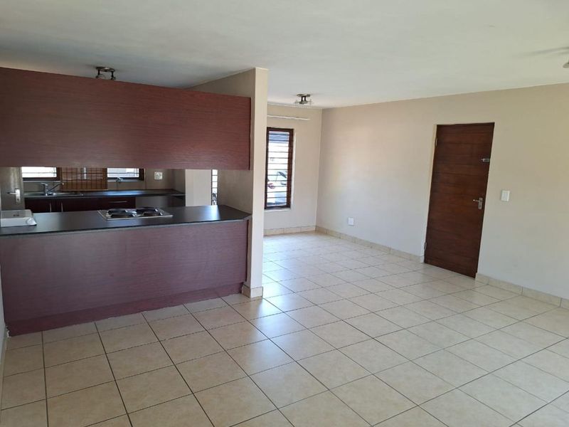 Open plan living area featuring tiled flooring and a functional kitchen with built-in cabinetry and hob, offering a clean and versatile space.