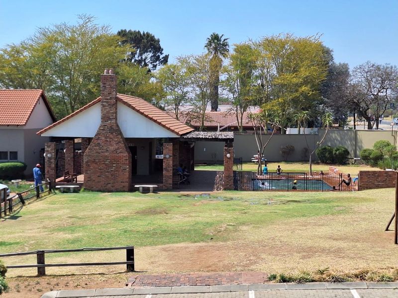 Communal outdoor area featuring a swimming pool, covered patio with a brick chimney, and landscaped garden space within a secure complex.
