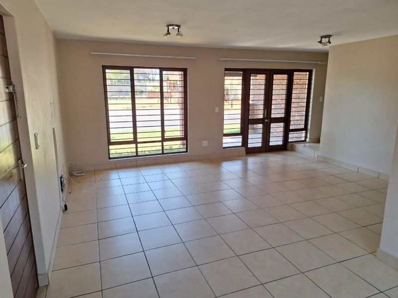 Spacious, empty living area featuring neutral tiled flooring, large windows with security bars, and double glass doors leading to the exterior.