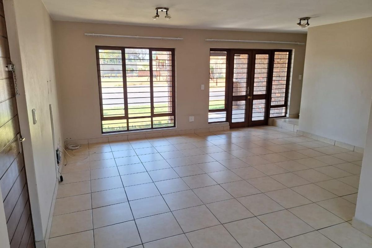 Spacious, empty living area featuring neutral tiled flooring, large windows with security bars, and double glass doors leading to the exterior.
