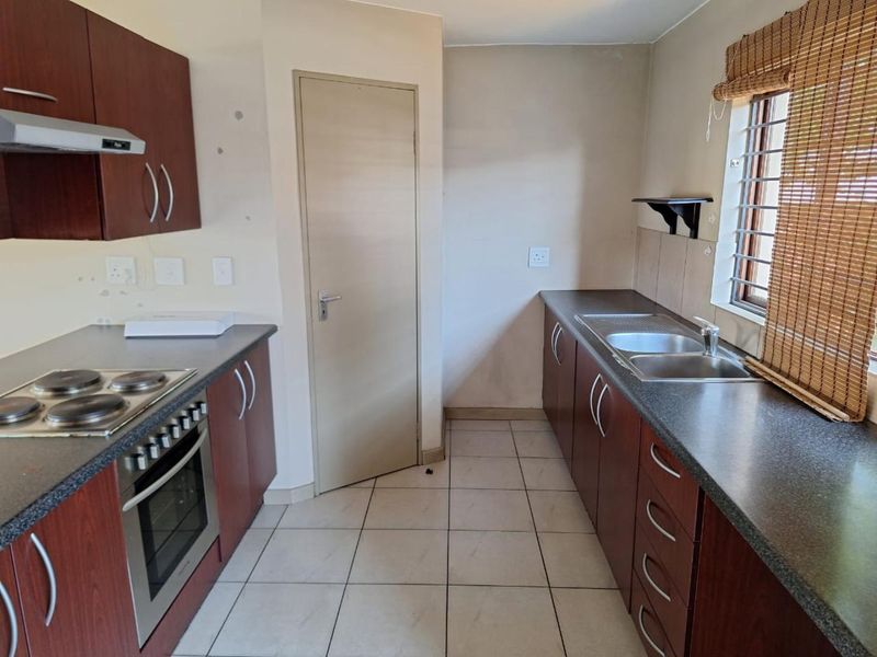 A functional galley-style kitchen featuring dark wood cabinetry, laminate countertops, a built-in oven with hob, and tiled flooring.