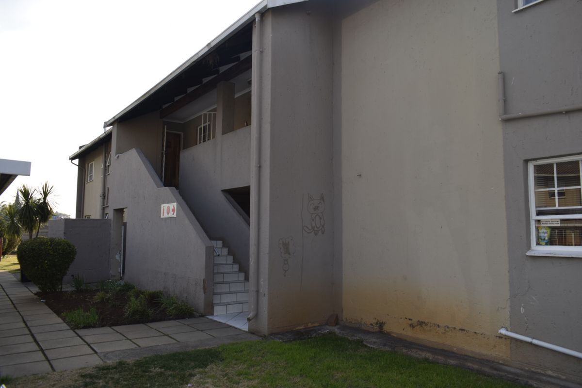 Exterior view of a townhouse complex showing a concrete staircase, paved walkway, and signs of exterior wall weathering and graffiti.