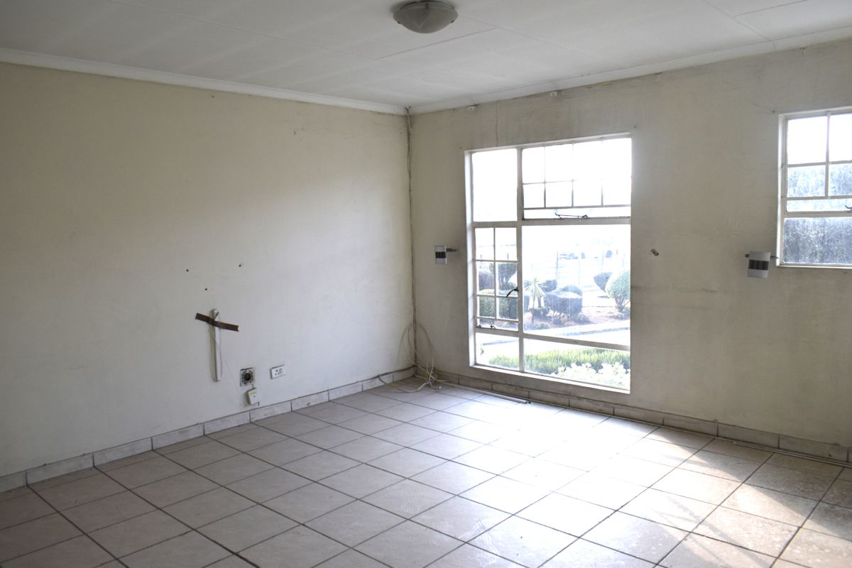 An empty living room featuring tiled flooring, steel-framed windows, and neutral walls, presenting a blank canvas ready for renovation and interior design updates.