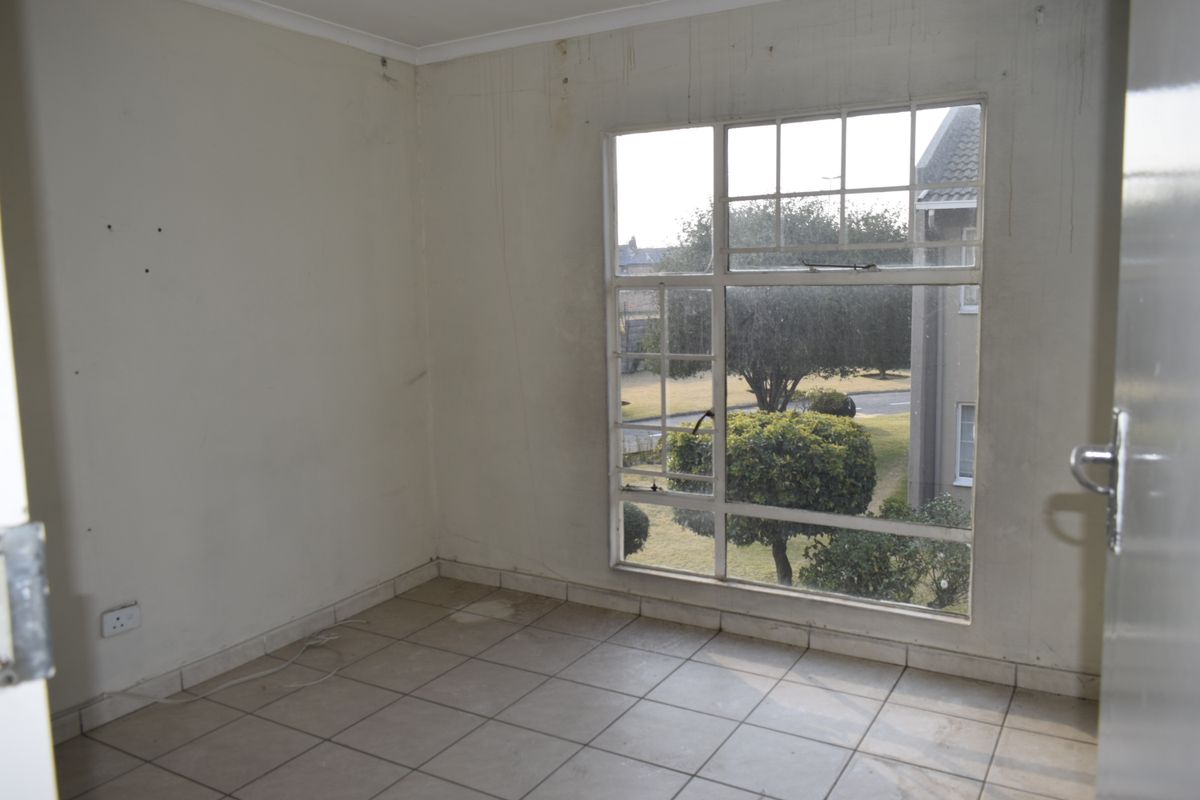 An empty bedroom featuring tiled flooring and a large window with views of the surrounding complex grounds.