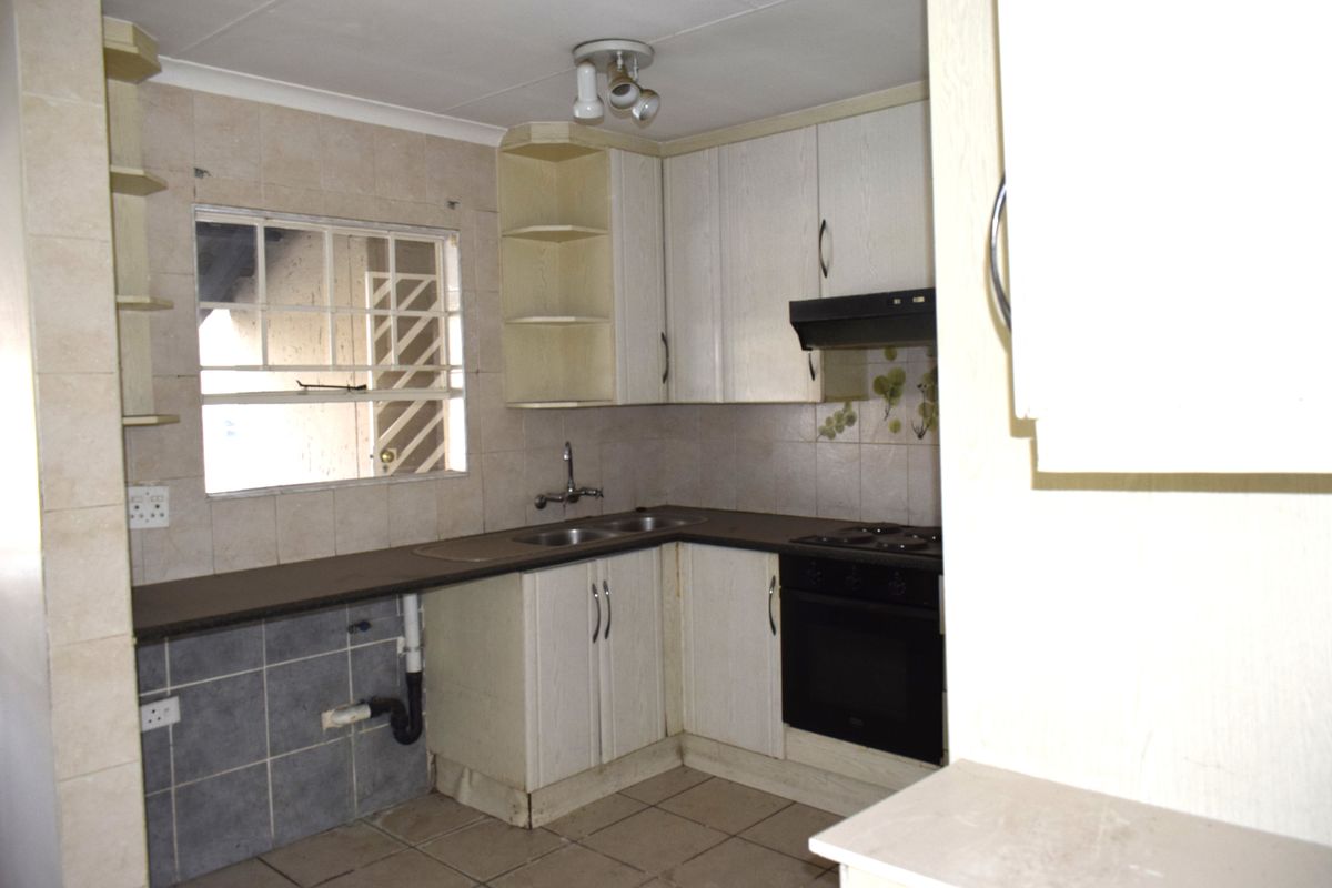 A dated kitchen featuring built-in cabinetry, a double sink, and integrated oven and hob, with tiled splashbacks and flooring throughout.