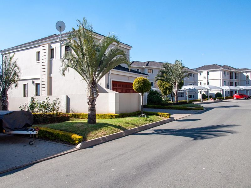 Street view of a townhouse complex featuring paved driveways, landscaped gardens, and covered carport parking areas.