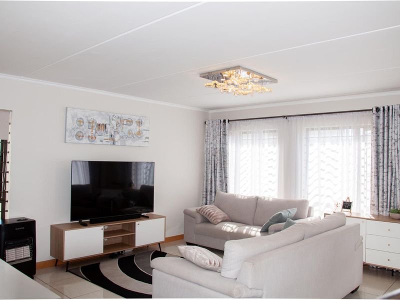 A bright and well-maintained living room featuring neutral tiled flooring, modern ceiling lighting, and large windows that provide ample natural light.
