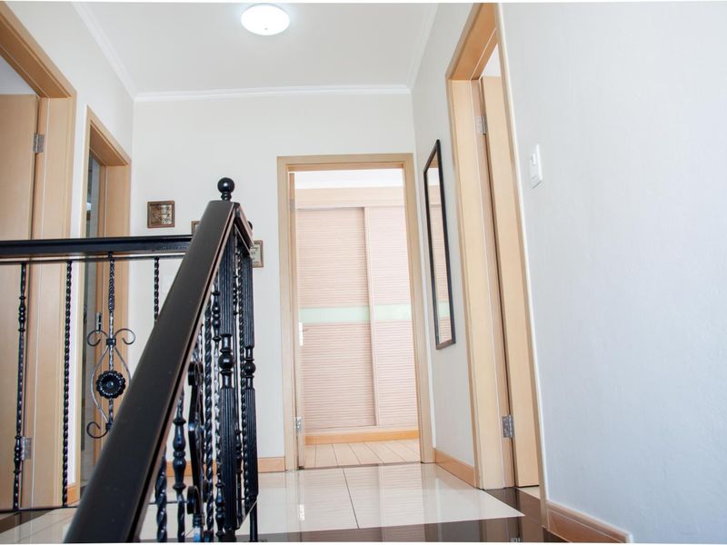 A bright upstairs landing area featuring tiled flooring, a decorative wrought iron balustrade, and access to adjacent bedrooms with built-in cabinetry.