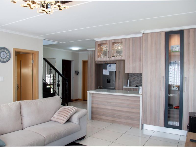 Open-plan living area featuring a modern kitchen with wood-grain cabinetry, a breakfast bar, and tiled flooring, seamlessly connected to the staircase and hallway.