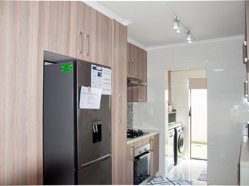 Modern kitchen featuring wood-grain cabinetry, stone countertops, integrated gas hob, oven, and extractor fan, with an adjacent scullery area and tiled flooring.