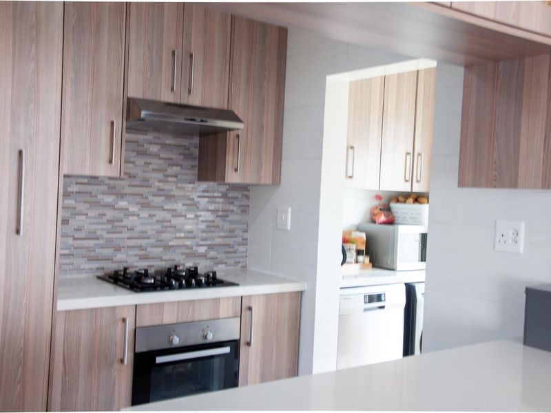 Modern kitchen featuring wood-look cabinetry, stone countertops, a gas hob, and an integrated oven, with an adjacent scullery area.