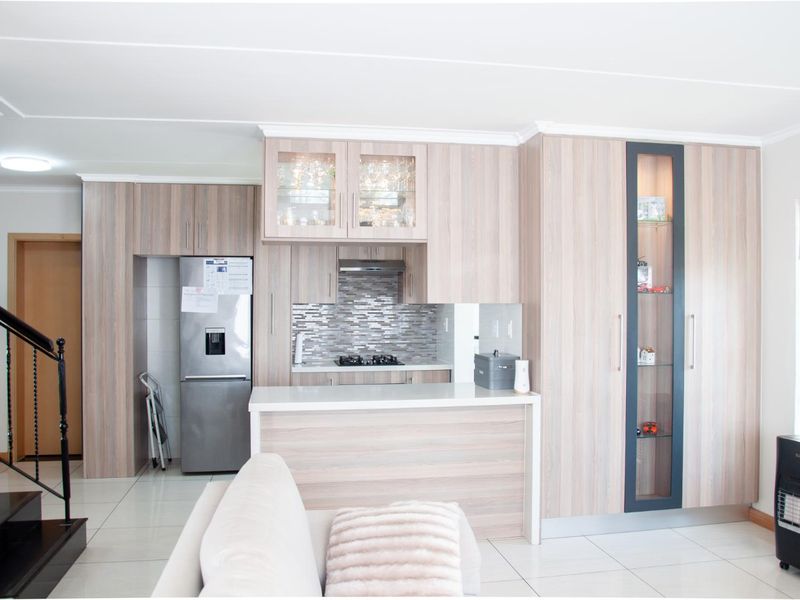 Modern open-plan kitchen featuring light wood-grain cabinetry, stone countertops, a gas hob, and integrated display shelving, seamlessly connected to the living area.