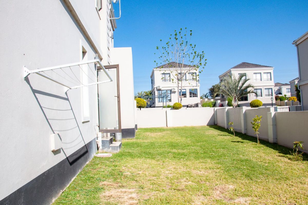 A private rear garden area featuring a well-maintained lawn, perimeter boundary walls, and a wall-mounted drying rack attached to the townhouse exterior.