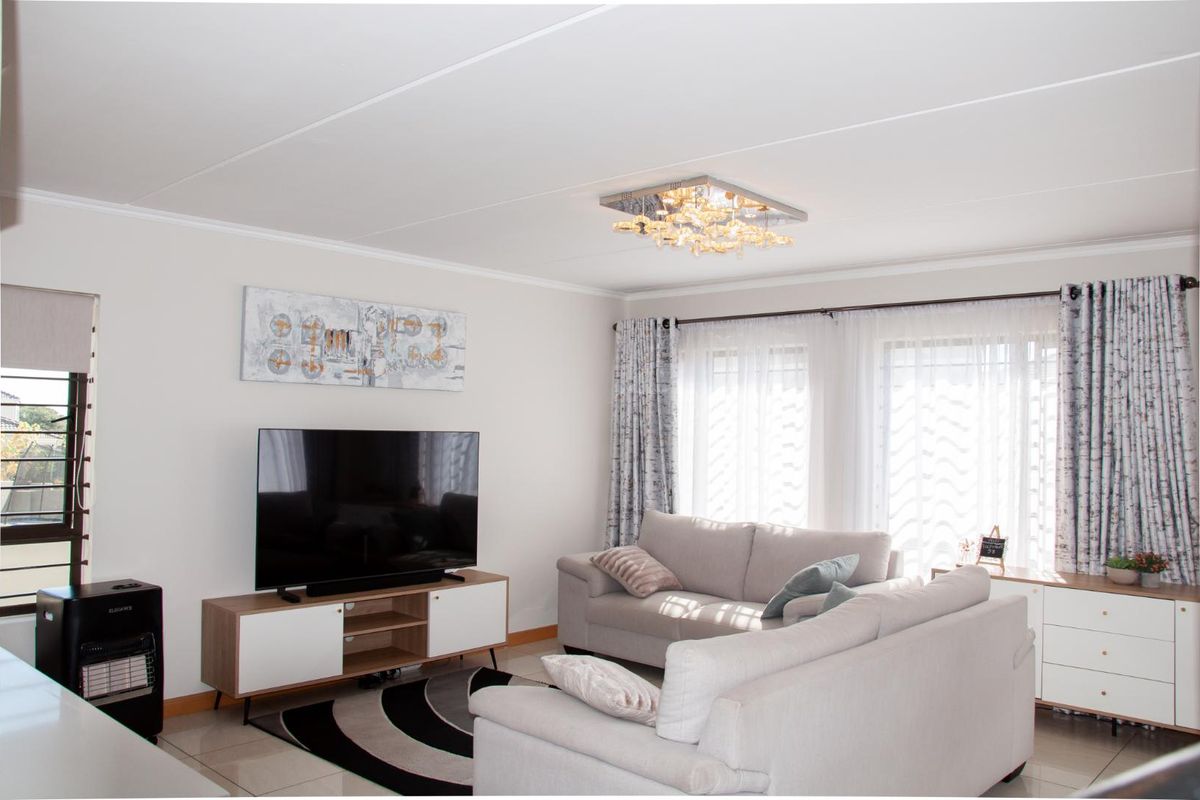 A bright and well-maintained living room featuring neutral tiled flooring, modern ceiling lighting, and large windows that provide ample natural light.