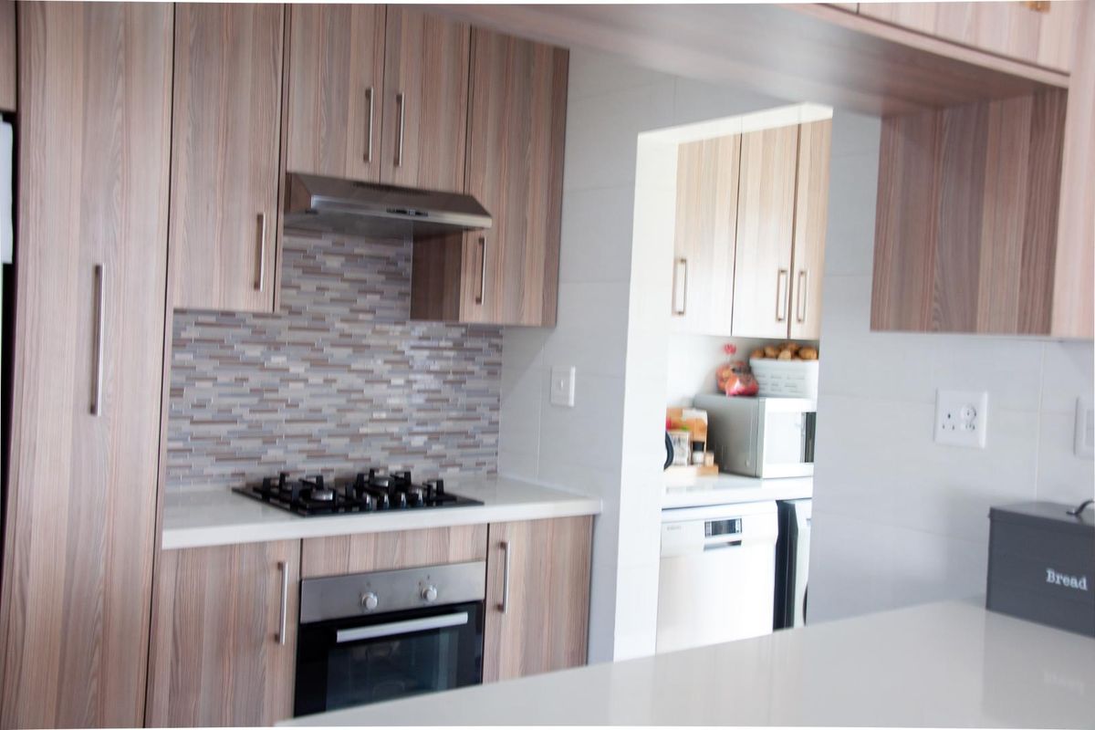 Modern kitchen featuring wood-look cabinetry, stone countertops, a gas hob, and an integrated oven, with an adjacent scullery area.