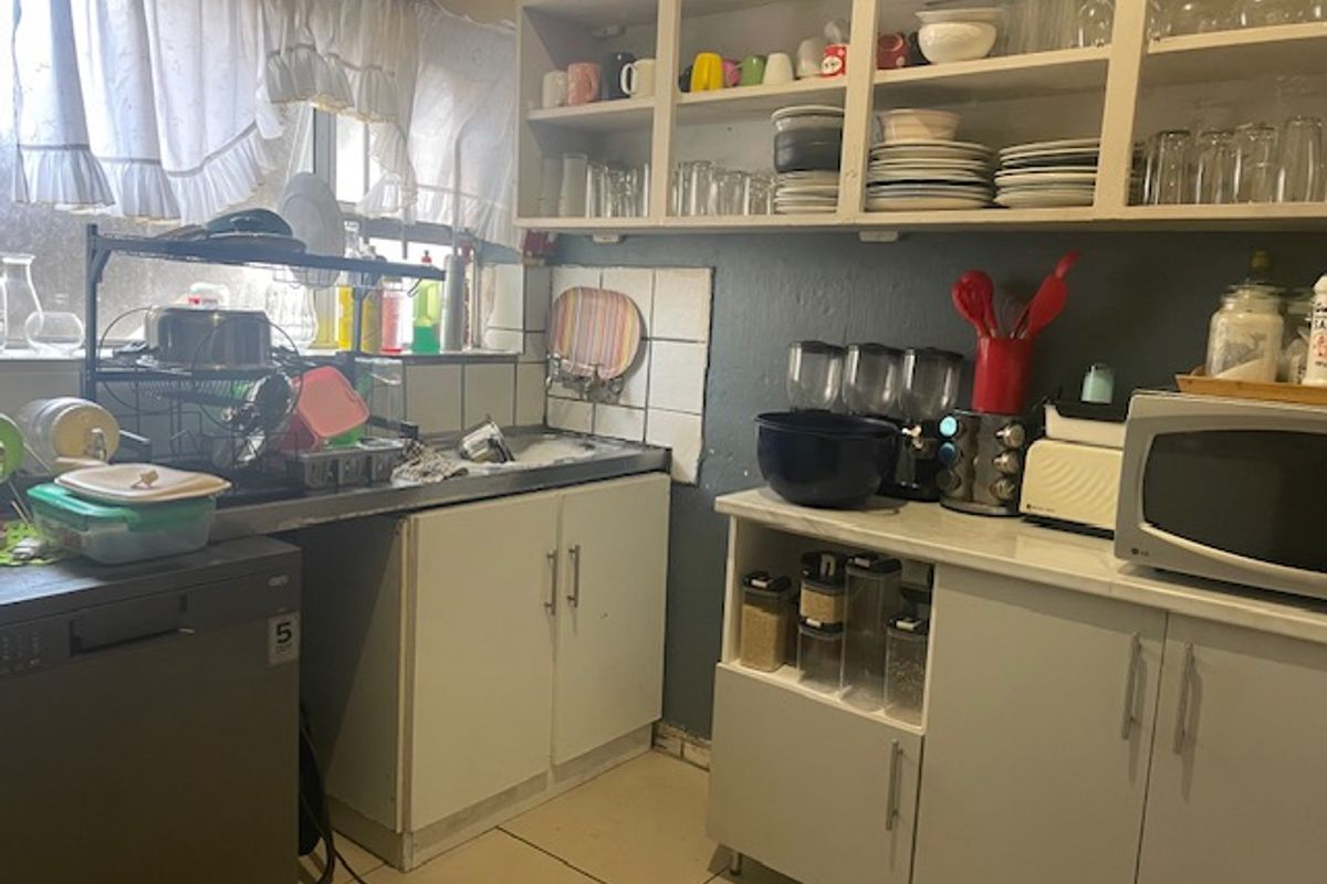 A compact kitchen featuring built-in cabinetry, open shelving, and a stainless steel sink, currently requiring cosmetic updates to improve functionality and aesthetic appeal.