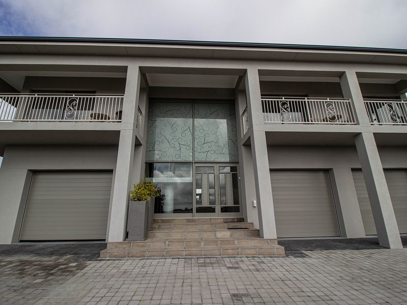 Modern double-story residence featuring a triple garage, decorative glass entrance, and upper-level balconies with wrought iron railings.