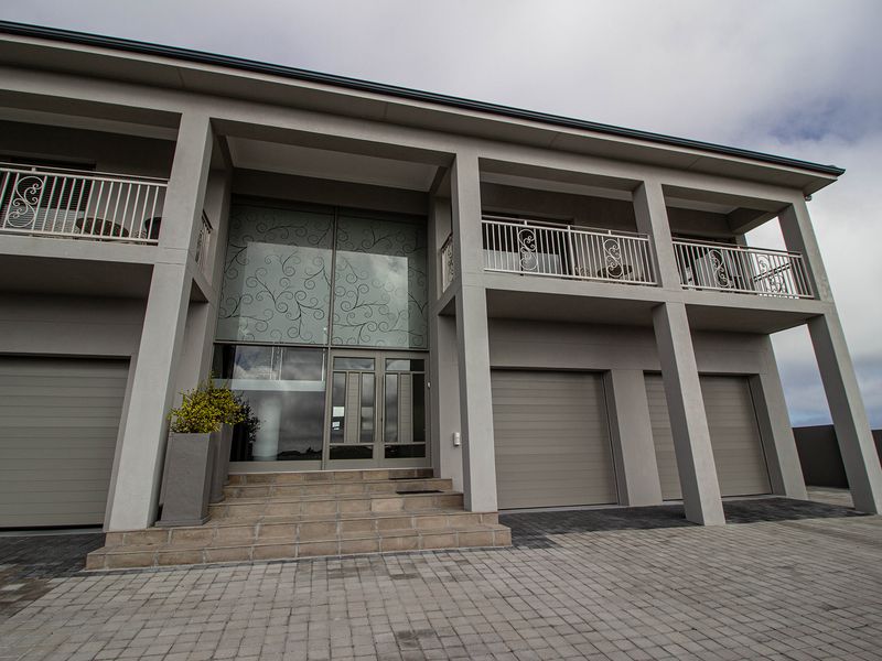Modern multi-level residential facade featuring a paved driveway, double garage, decorative glass entrance, and upper-level balconies with wrought iron railings.
