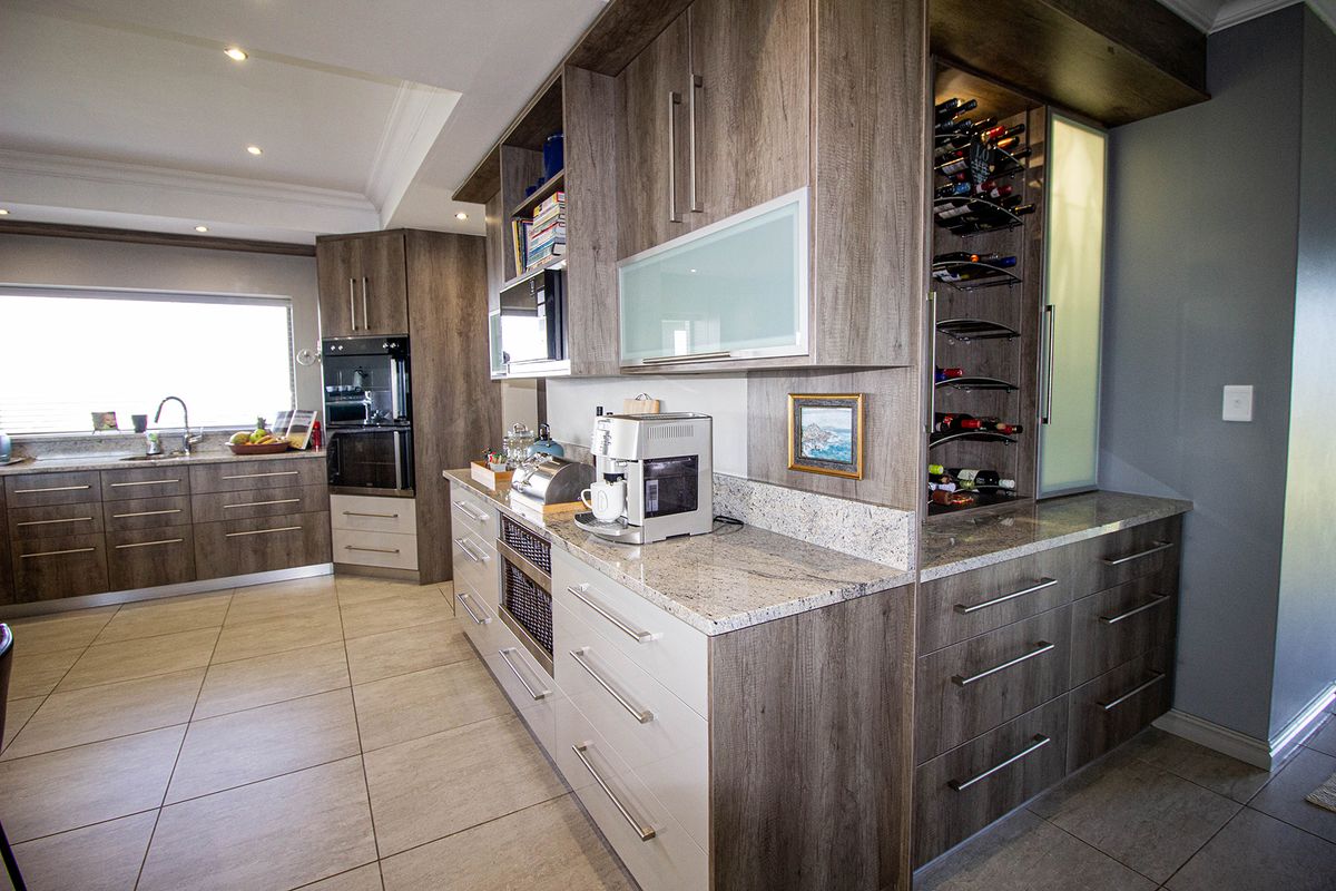 Modern kitchen featuring wood-grain cabinetry, granite countertops, built-in appliances, and a dedicated wine storage rack, complemented by neutral tiled flooring and recessed lighting.