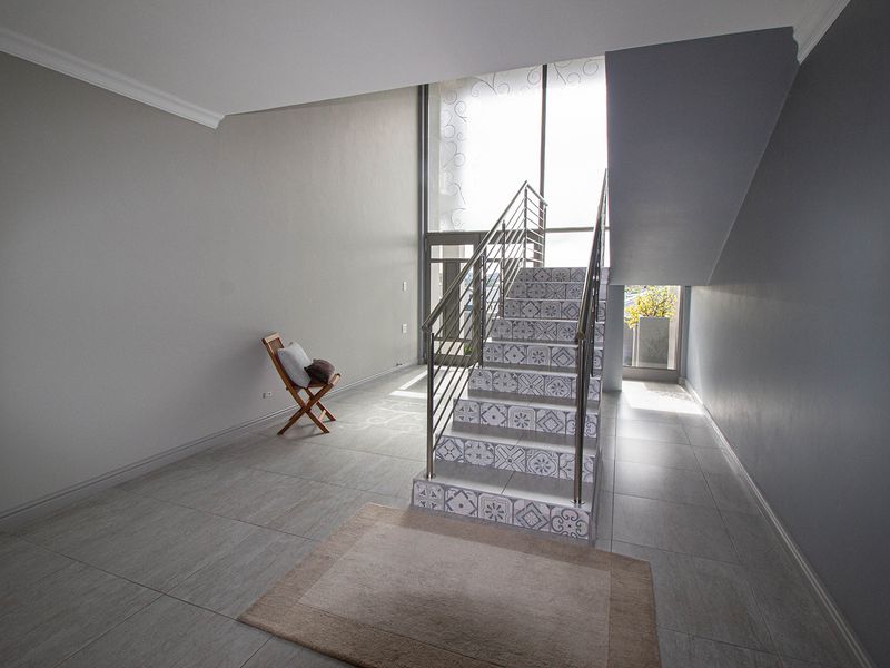Spacious entrance hall featuring a decorative tiled staircase with stainless steel balustrade, large windows for natural light, and neutral porcelain floor tiles.