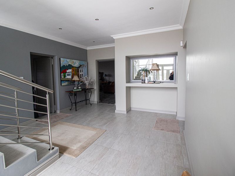 Spacious entrance hall featuring modern tiled flooring, recessed downlighting, a built-in wall niche, and a contemporary stainless steel staircase railing.