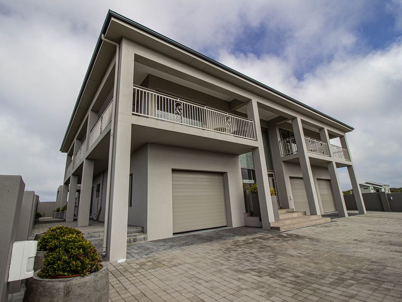Modern double-story residence featuring a triple garage, paved driveway, and expansive upper-level balconies with decorative wrought iron railings.