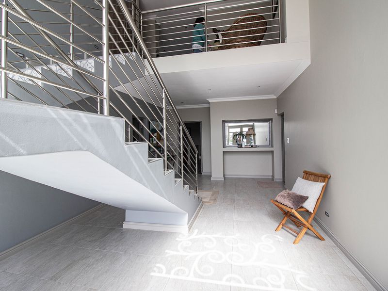 Spacious entrance hall featuring modern tiled flooring, a striking staircase with stainless steel railings, and an open mezzanine level overlooking the foyer.