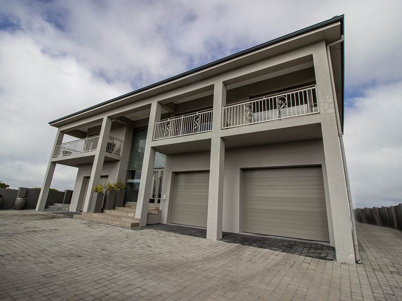 Modern two-story residential facade featuring a double garage, paved driveway, and upper-level balconies with decorative wrought iron railings.