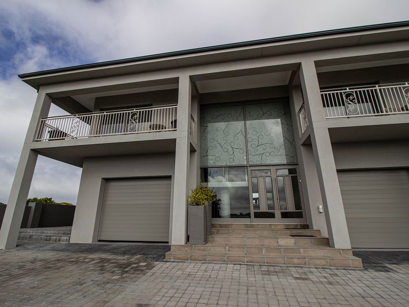 Modern two-story residential facade featuring double garage doors, upper-level balconies, and a prominent central entrance with decorative glass detailing.