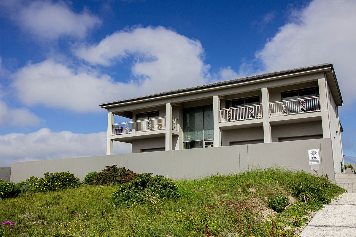 Rear elevation of a modern two-story house featuring upper-level balconies with decorative railings and a solid perimeter wall.