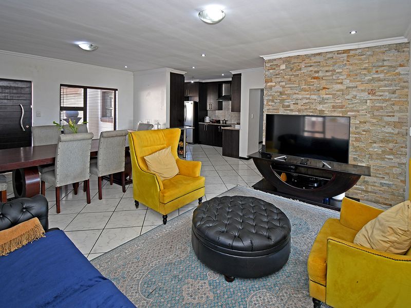 Open-plan living and dining area featuring a stone accent wall, tiled flooring, and a modern kitchen with dark cabinetry.