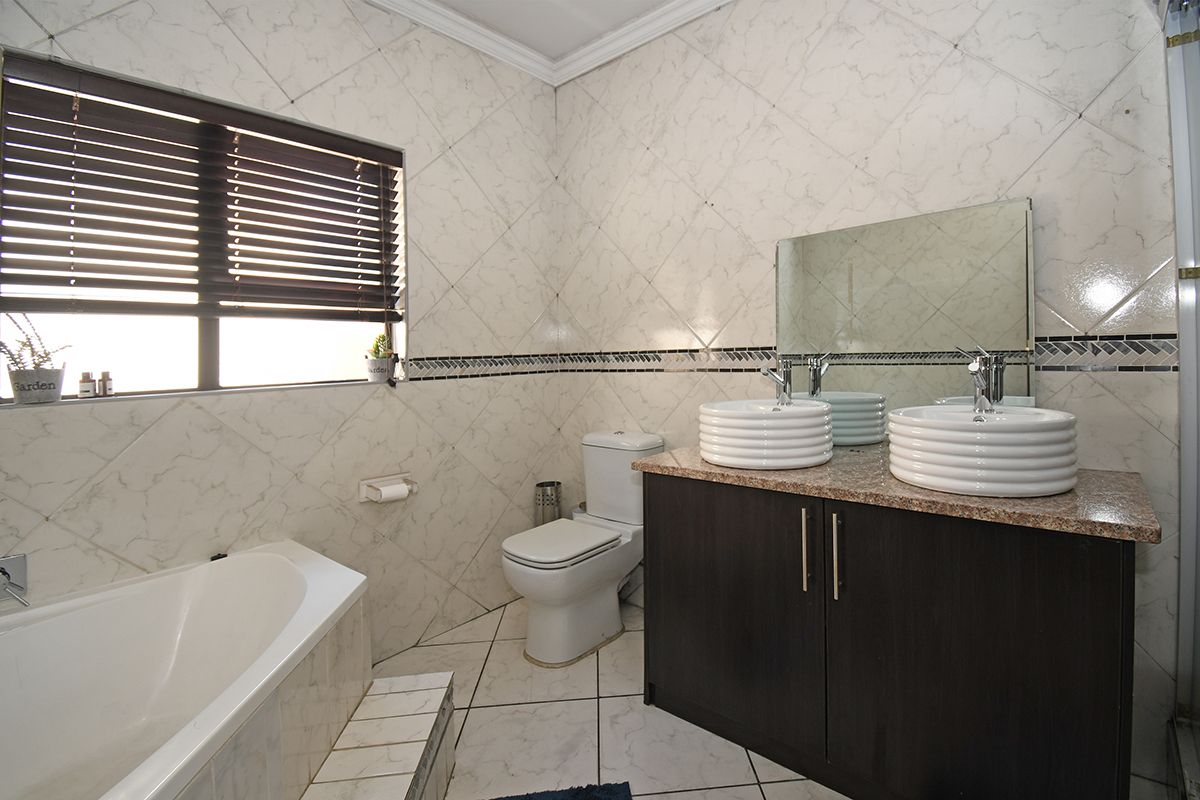 A well-maintained bathroom featuring a double vanity with vessel sinks, granite countertop, bathtub, and tiled finishes throughout.