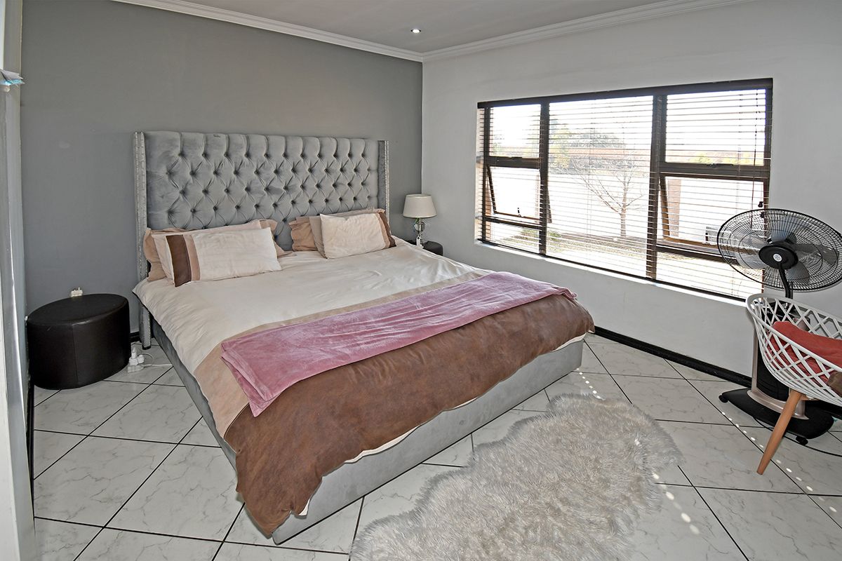 A bedroom featuring tiled flooring, a large window with venetian blinds, and a grey accent wall.