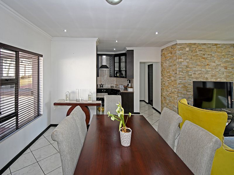 Open-plan living and dining area featuring a stone-clad feature wall, tiled flooring, recessed lighting, and a compact kitchen with built-in cabinetry.