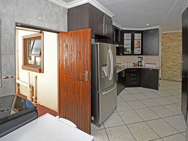 A functional kitchen featuring dark cabinetry, stone countertops, tiled flooring, and a decorative stone feature wall, with direct access to an outdoor area.