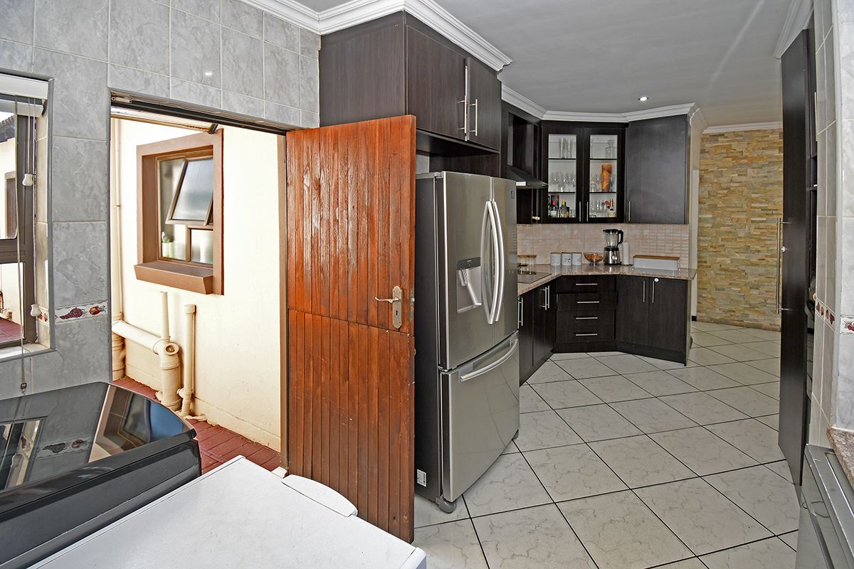 A functional kitchen featuring dark cabinetry, stone countertops, tiled flooring, and a decorative stone feature wall, with direct access to an outdoor area.