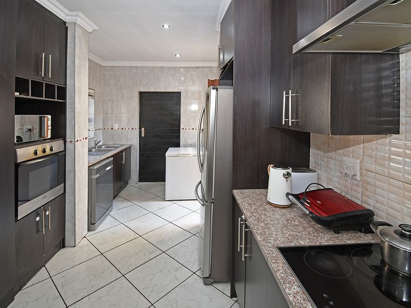 A functional kitchen featuring dark cabinetry, granite countertops, built-in oven, electric hob, extractor fan, and tiled flooring with a neutral backsplash.