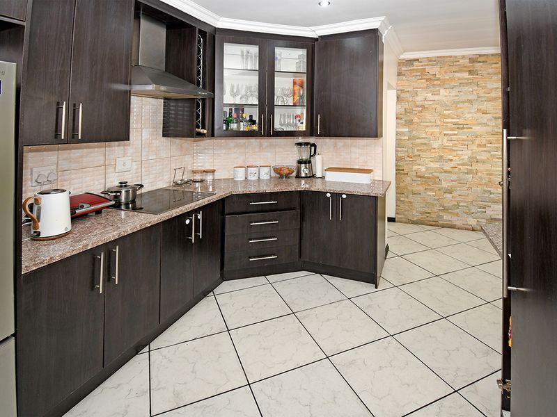 A well-maintained kitchen featuring dark wood cabinetry, granite countertops, an electric hob, and a decorative stone feature wall with tiled flooring.