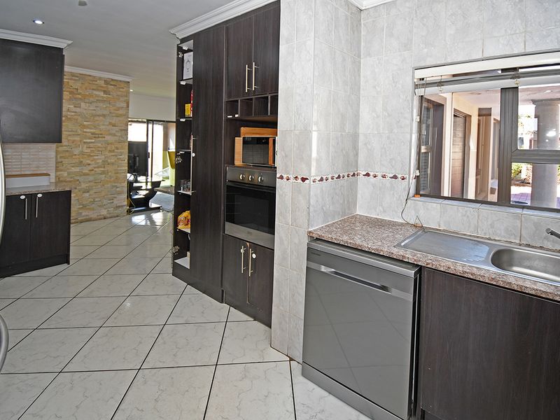 A functional kitchen featuring dark cabinetry, granite countertops, tiled flooring, and a stone feature wall, flowing into an open-plan living area.
