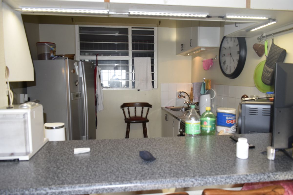 A functional kitchen featuring laminate countertops, built-in cabinetry, and a tiled splashback, with a pass-through window overlooking the living area.