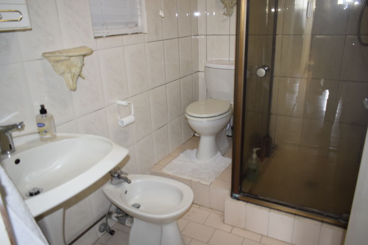 A compact bathroom featuring a pedestal basin, bidet, toilet, and a glass-enclosed shower with dated wall and floor tiling.