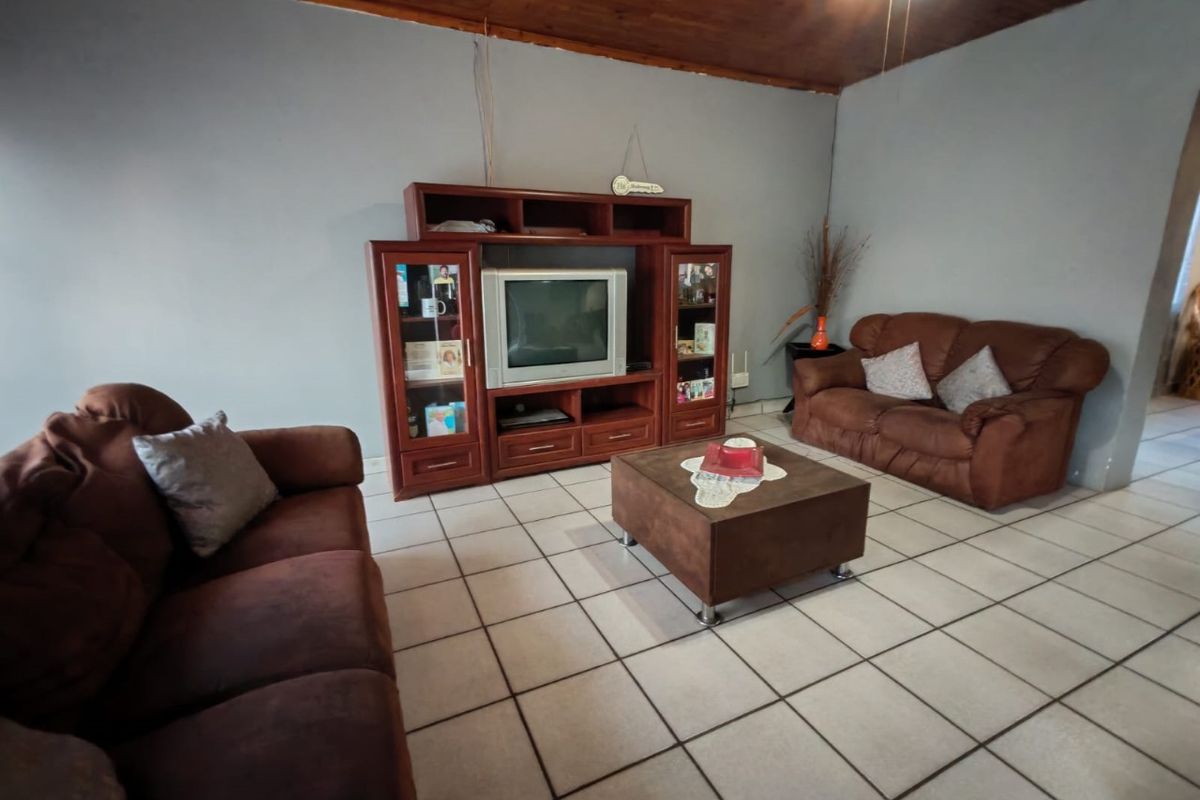 A living room featuring ceramic floor tiles and a rustic exposed timber ceiling, offering a dated aesthetic ready for modernization.