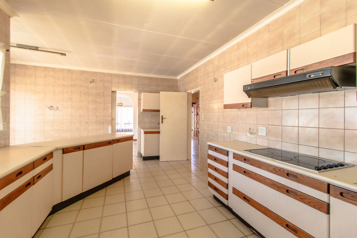 A functional kitchen featuring tiled walls and flooring, built-in cabinetry, a fitted electric hob, and an integrated extractor fan.